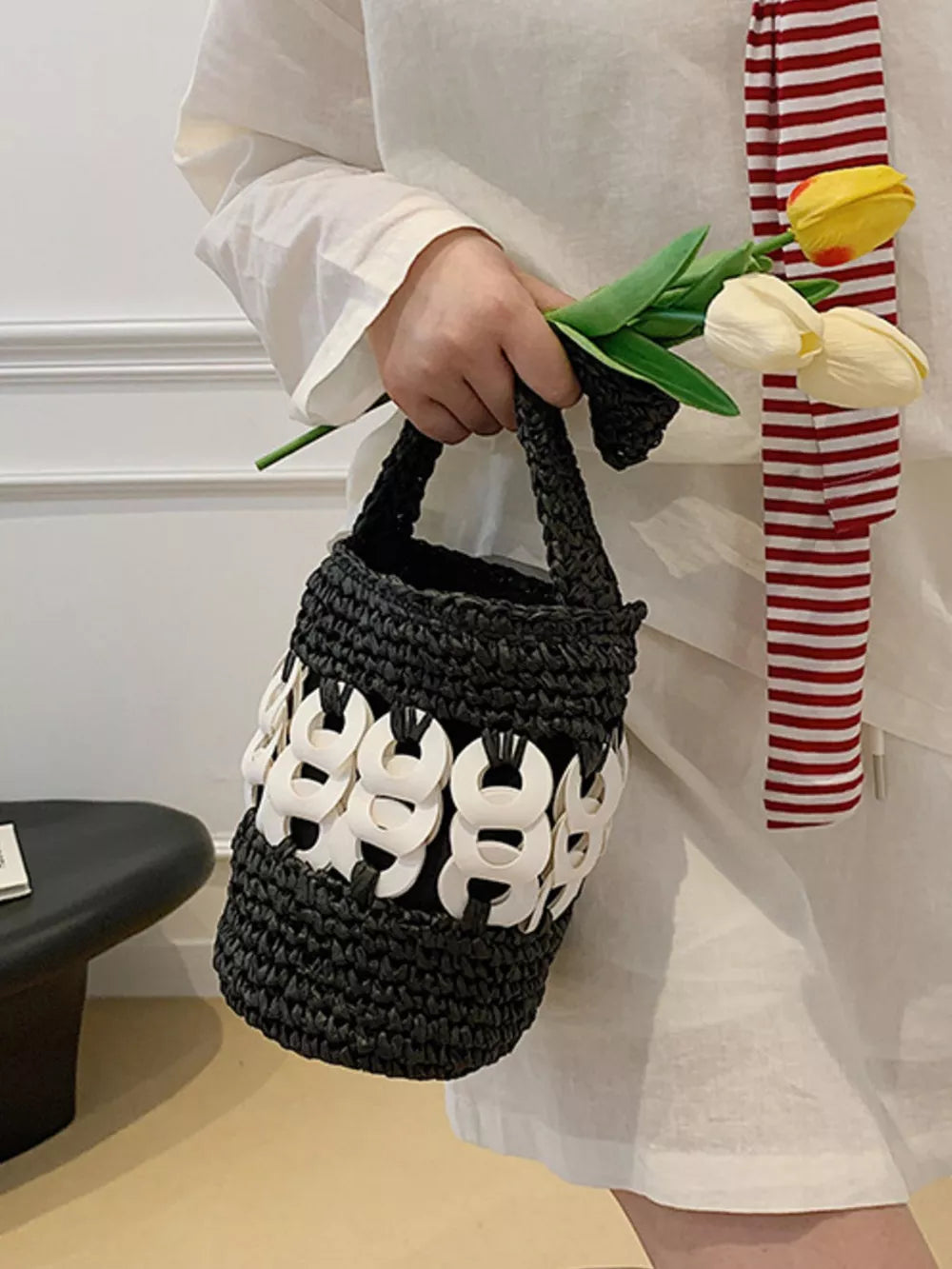 Black woven straw bucket tote with white chain detail.