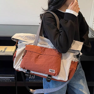 Tote bag in rust, cream, and grey colorblock nylon with adjustable straps and buckle details.