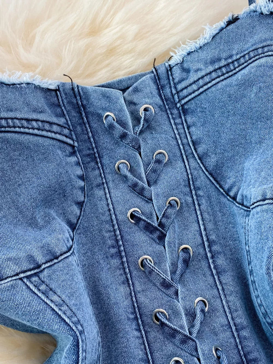 Blue denim corset dress with lace-up front and frayed hem detail.