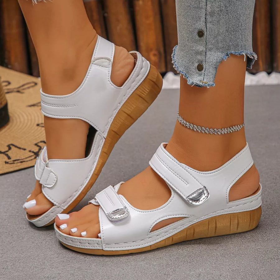 White adjustable wedge sandals with hook-and-loop straps and a wooden-look sole.