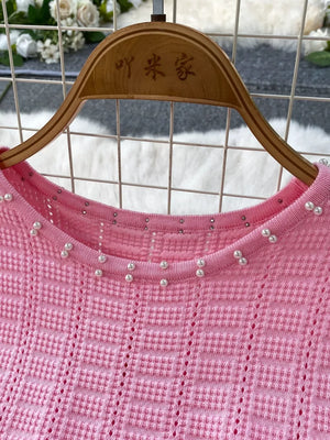 Pink knit midi dress with pearl and rhinestone neckline detail and cutout pattern.