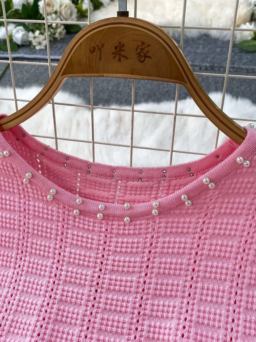 Pink knit midi dress with pearl and rhinestone neckline detail and cutout pattern.