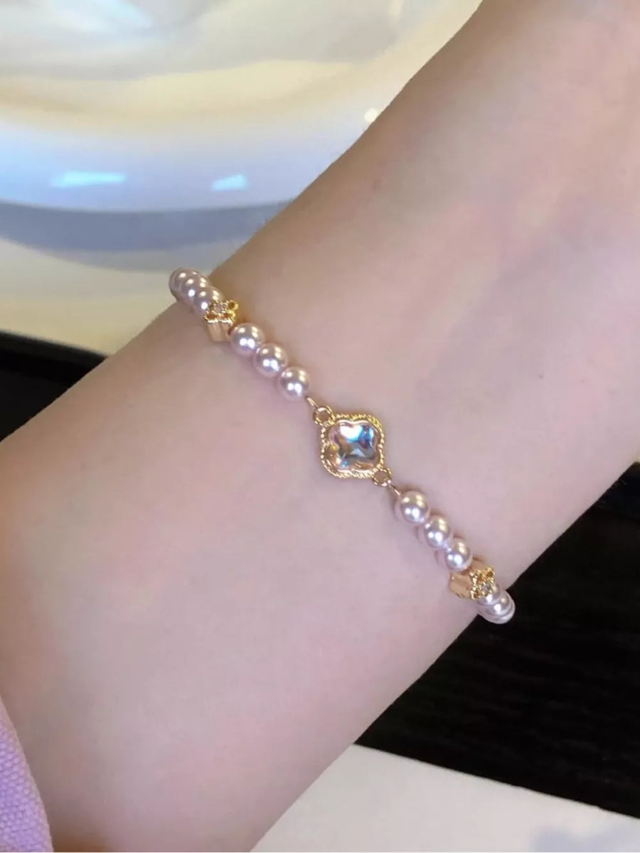 Delicate pearl bracelet with gold clover charms and a central crystal charm.