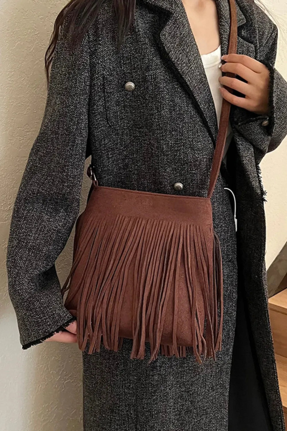 Brown suede crossbody bag with fringe detail and adjustable strap.