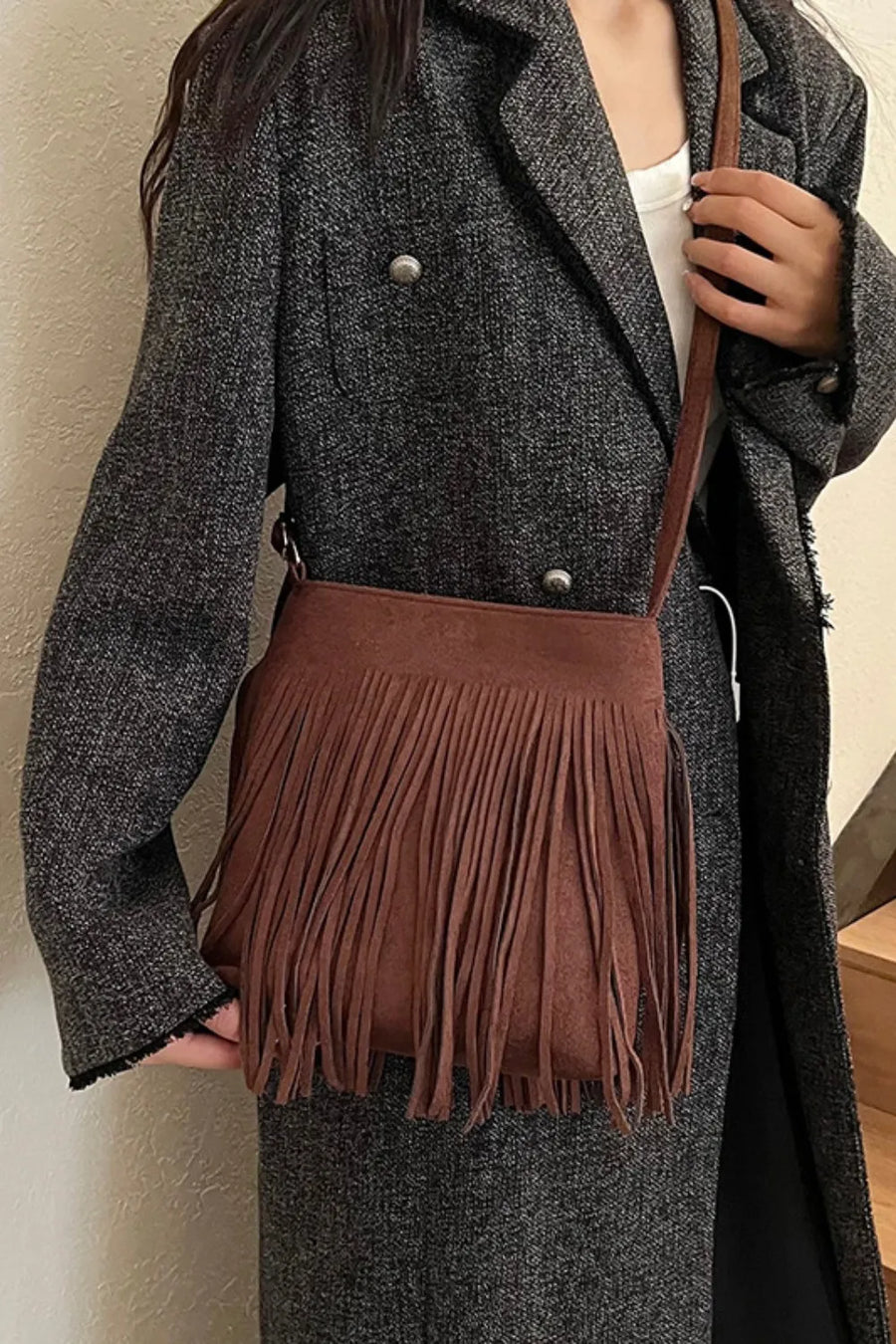 Brown suede crossbody bag with fringe detail and adjustable strap.