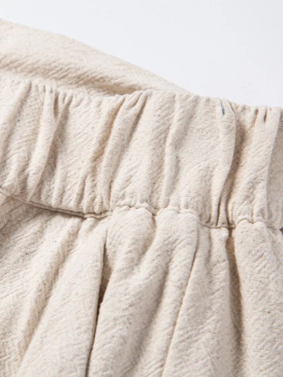 Beige linen drawstring trousers with elastic waistband and subtle herringbone texture.