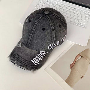 Grey distressed baseball cap with white "NEVER GIVE UP" embroidery and frayed details.