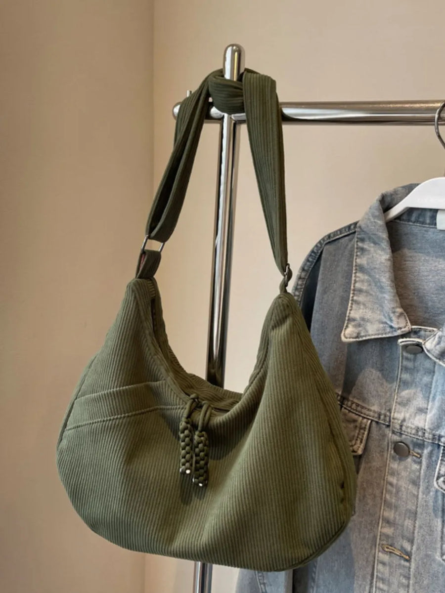 Moss green corduroy crescent shoulder bag with braided tassels and front pocket.