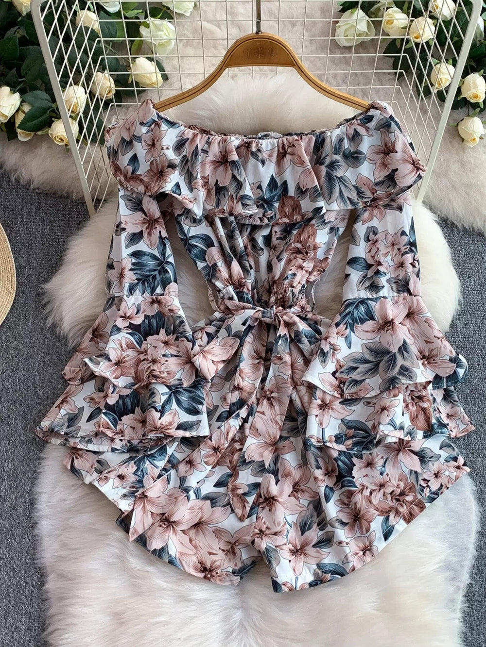 Off-shoulder ruffled romper with floral print, bow tie waist, and bell sleeves.
