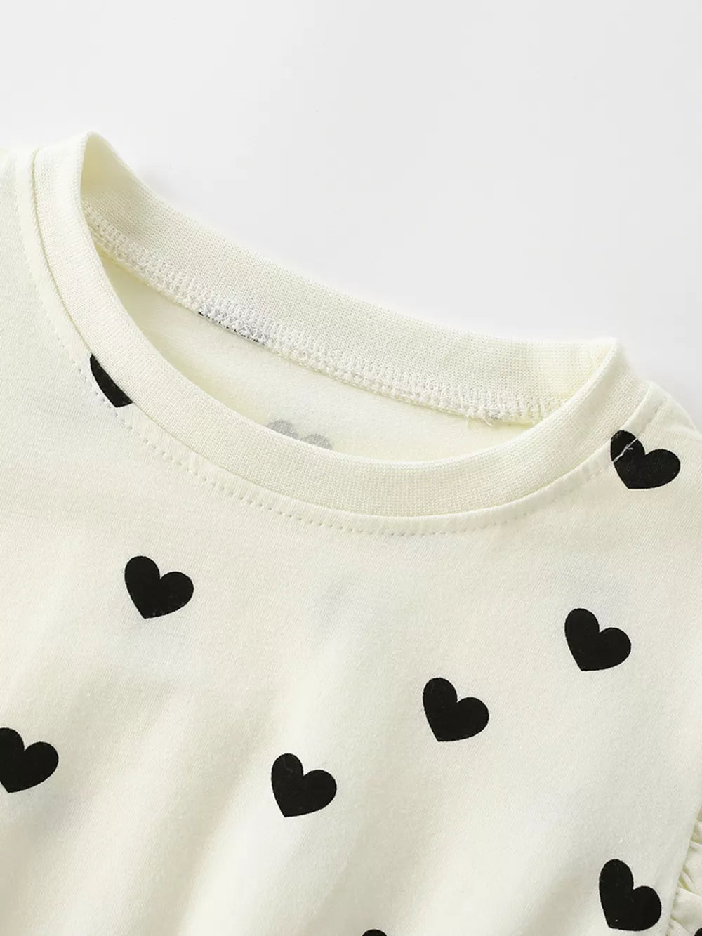 Children's cream dress with black heart print and ruffle sleeve detail.