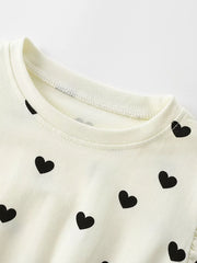 Children's cream dress with black heart print and ruffle sleeve detail.