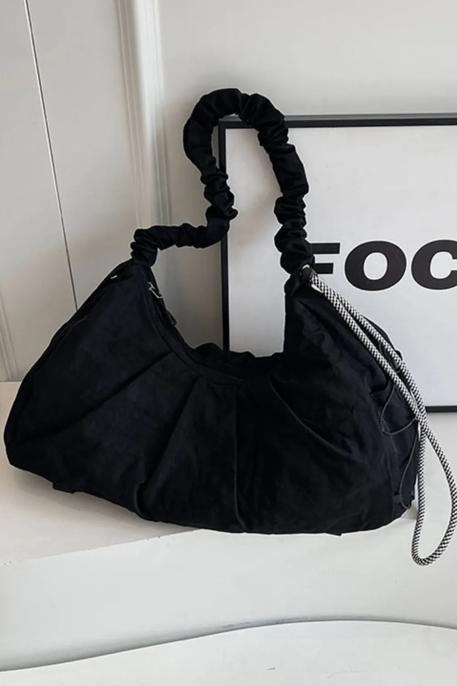 Black gathered crescent shoulder bag with ruched strap and checkered cord detail