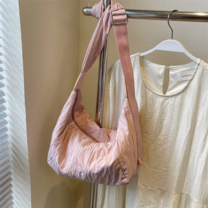 Pink quilted crescent shoulder bag with adjustable strap and zipper detail.