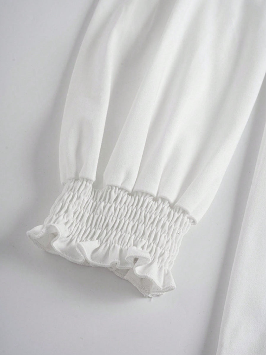 White tunic top with smocked ruffled cuffs and voluminous sleeves.