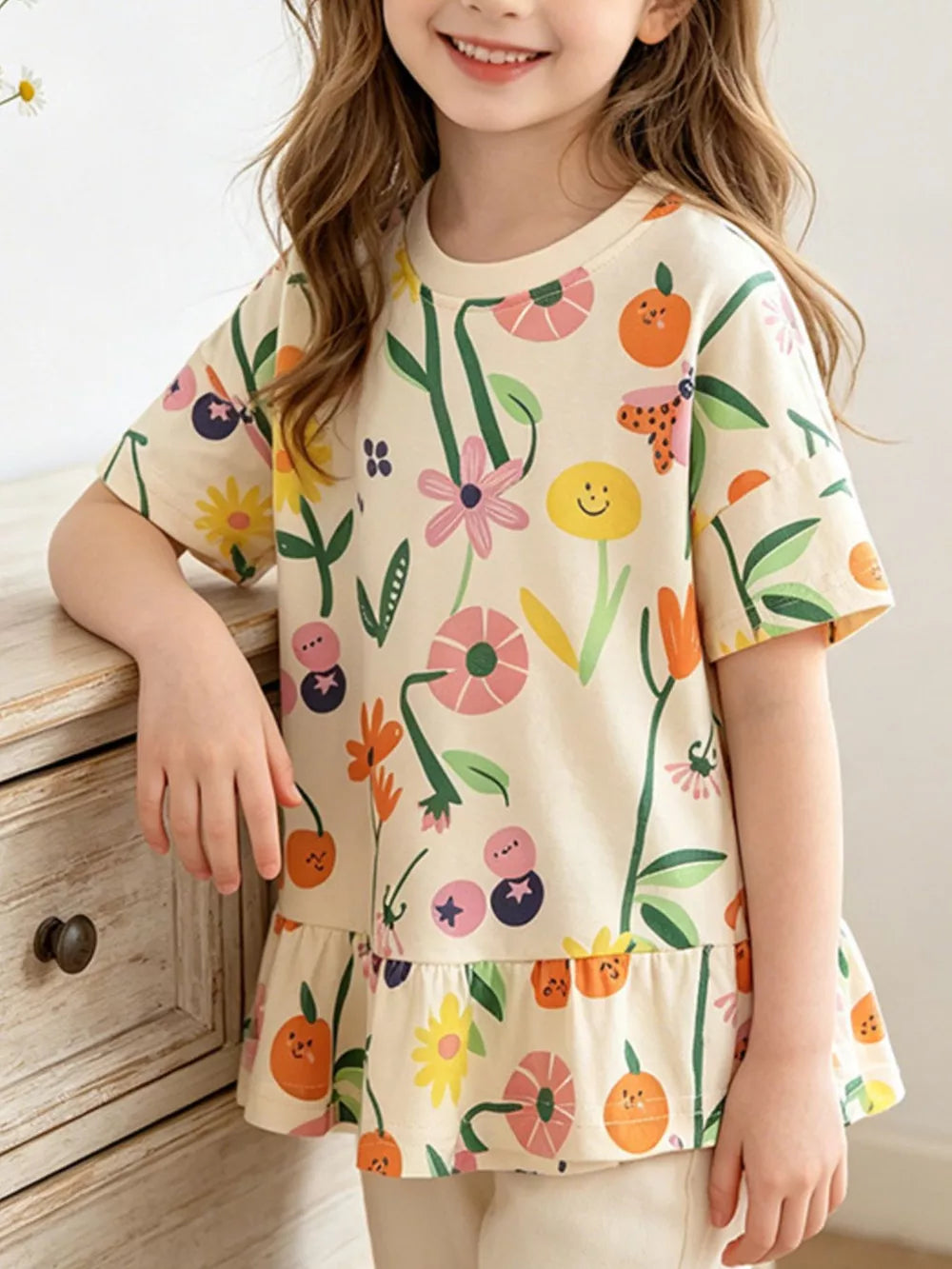 Baby t-shirt with whimsical floral and fruit print, short sleeves, and ruffled hem.