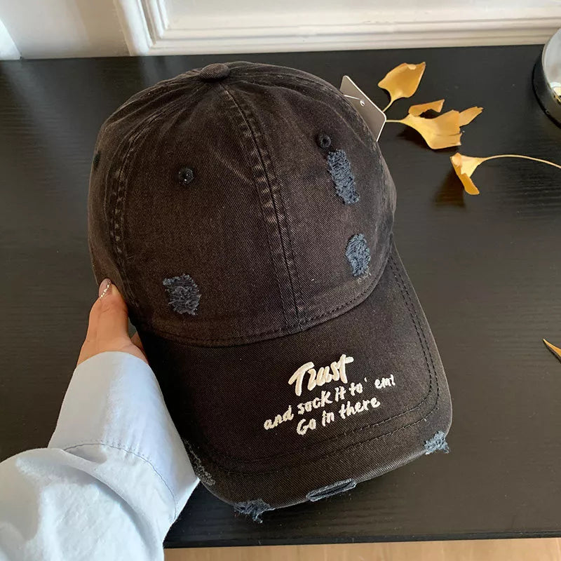 Black distressed baseball cap with white embroidered text and frayed details.