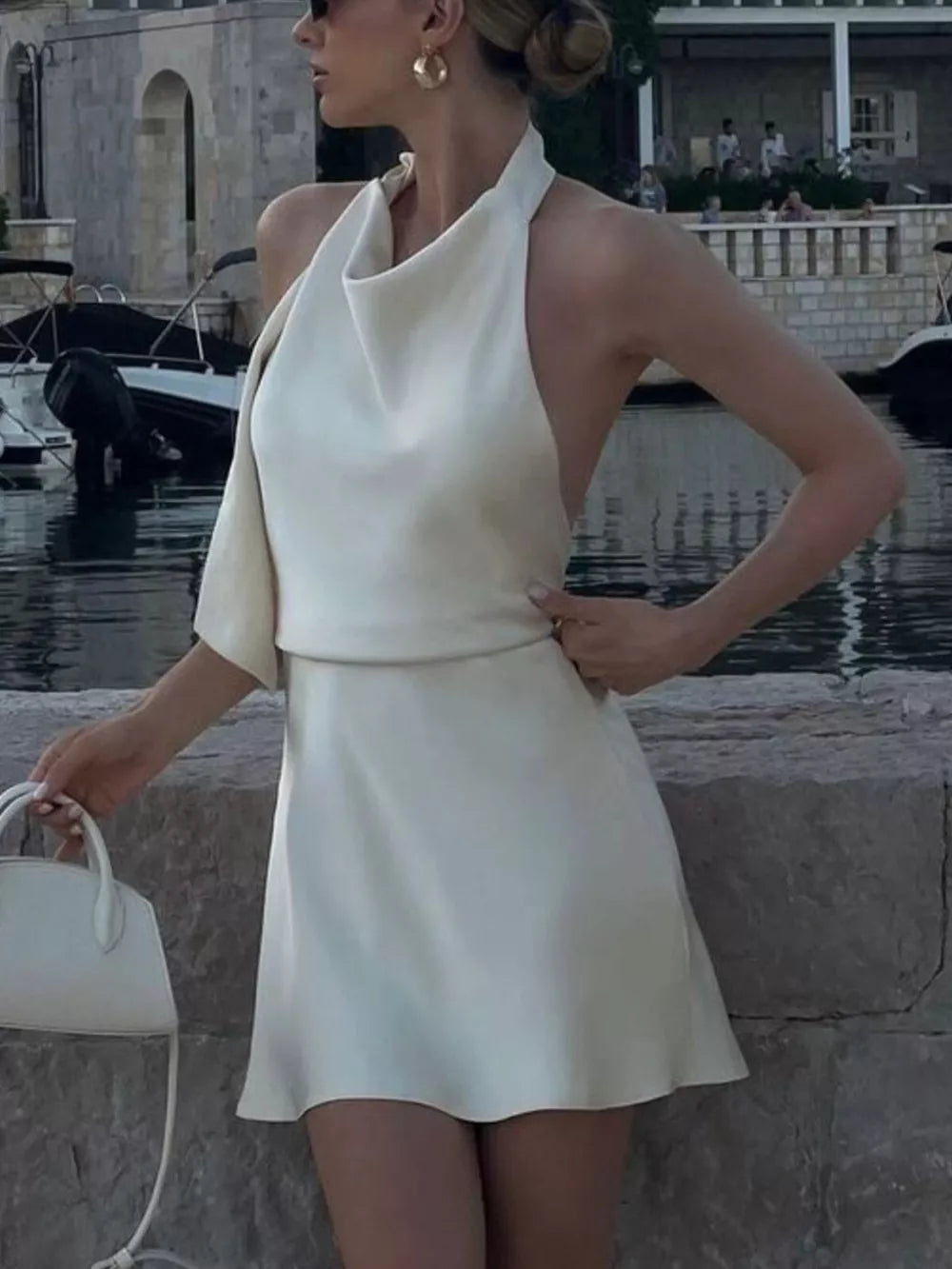 Cream halter neck mini dress with cowl detail and draped sleeves.