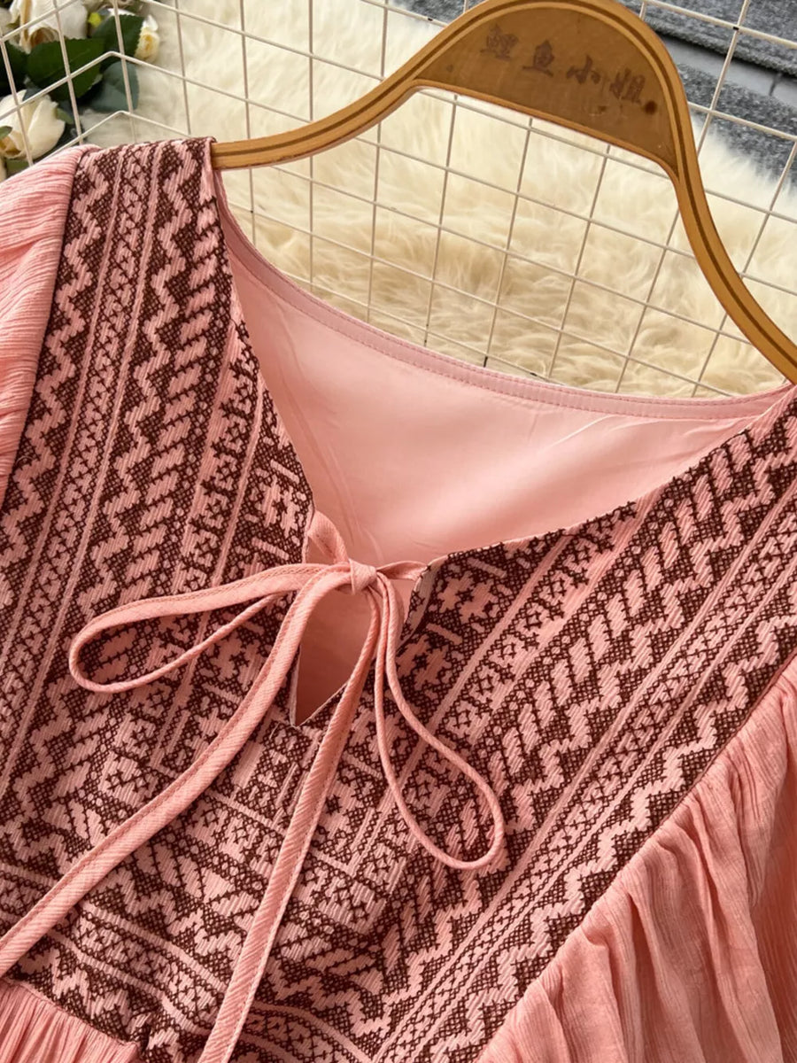 Pink embroidered V-neck maxi dress with tie detail and textured fabric.