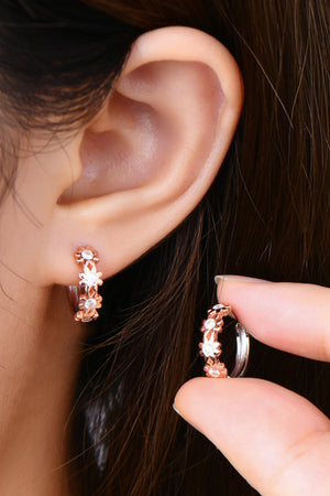 Rose gold huggie hoop earrings with floral embellishments and clear stones.