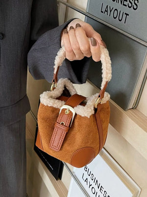 Brown suede bucket bag with fuzzy trim and leather buckle detail.