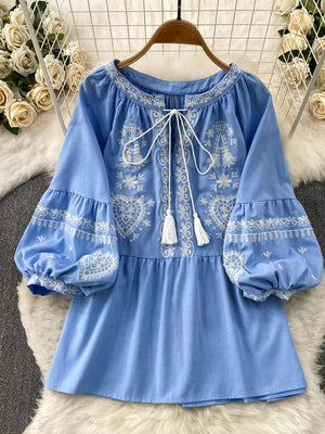 Blue embroidered tie-neck blouse with balloon sleeves and tassel details.