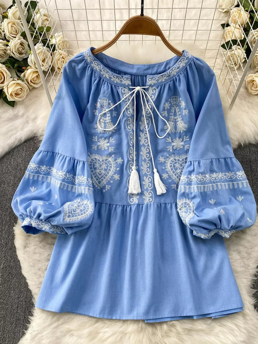Blue embroidered tie-neck blouse with balloon sleeves and tassel details.