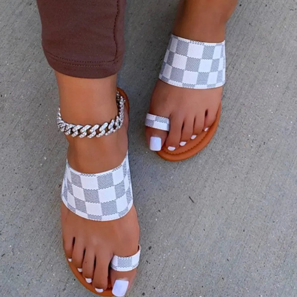 White checkered toe-loop flat sandals with brown soles and a silver anklet.