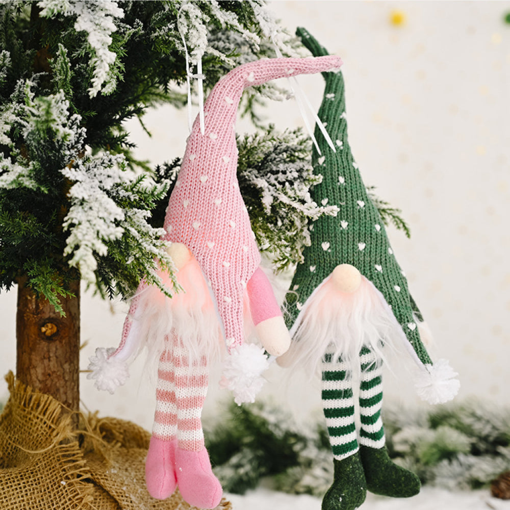 Knitted gnome ornaments in blush pink with heart pattern and green with heart pattern hang on a tree.