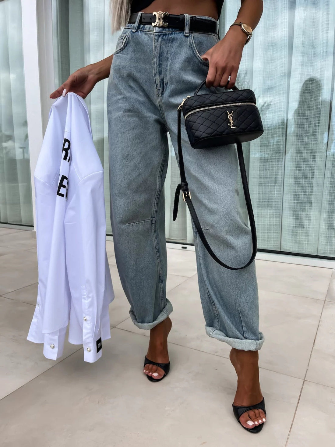 Baggy light wash denim barrel leg jeans with cuffed hems, worn with black heels and a quilted handbag.
