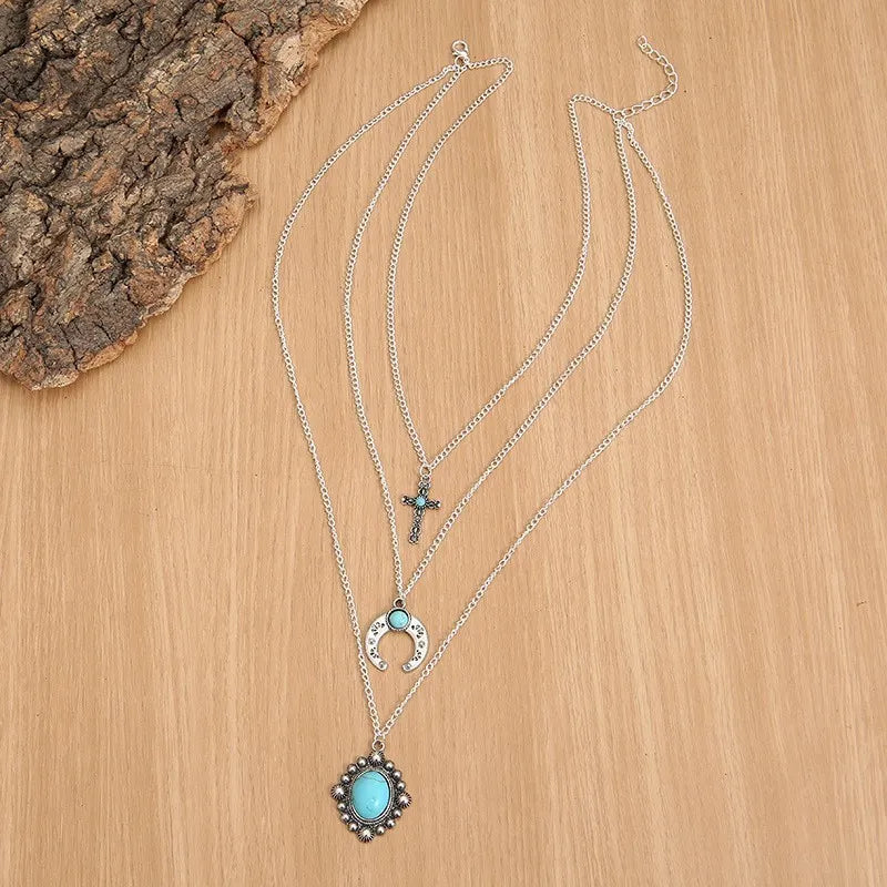 Silver layered pendant necklace with turquoise cross, crescent moon, and oval stone charms.
