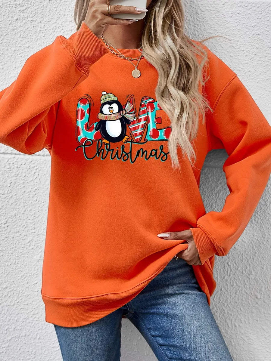 Orange crewneck sweatshirt with festive penguin and "Love Christmas" graphic.