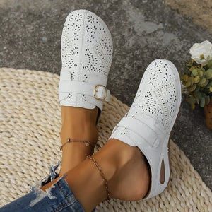 White laser-cut buckle mule wedges with decorative perforations and adjustable strap.