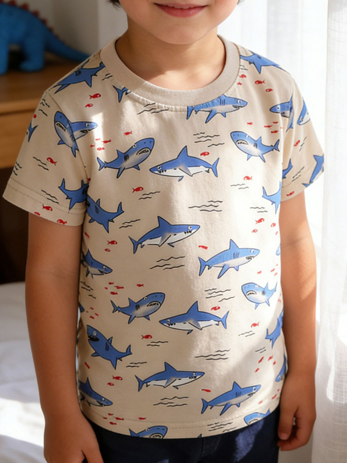 Toddler crew neck t-shirt with allover blue shark and red fish print on a tan background.