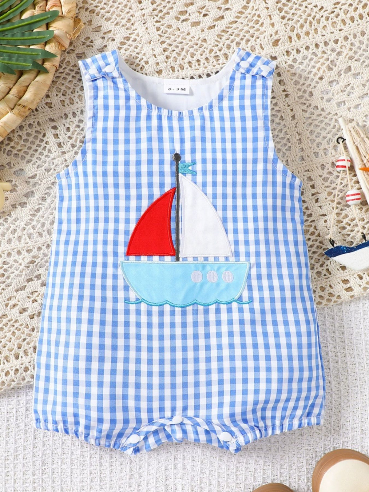 Blue gingham baby one-piece with sailboat appliqué, sleeveless, round neck, comfortable fit.