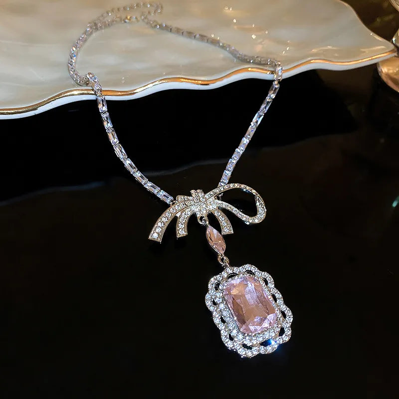 Silver bow pendant necklace with crystal accents and a large pink gemstone drop.