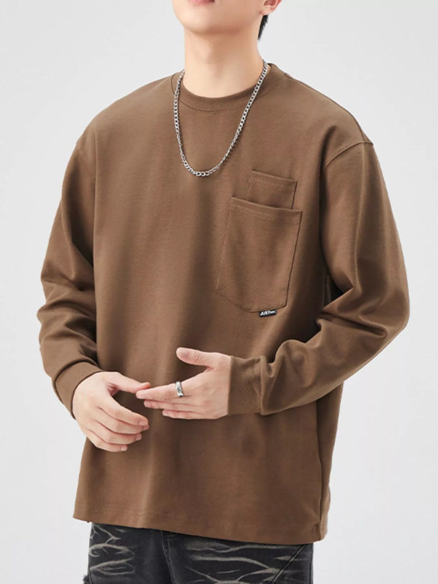 Brown long-sleeve sweatshirt with chest pocket and crewneck, styled with a chain necklace.