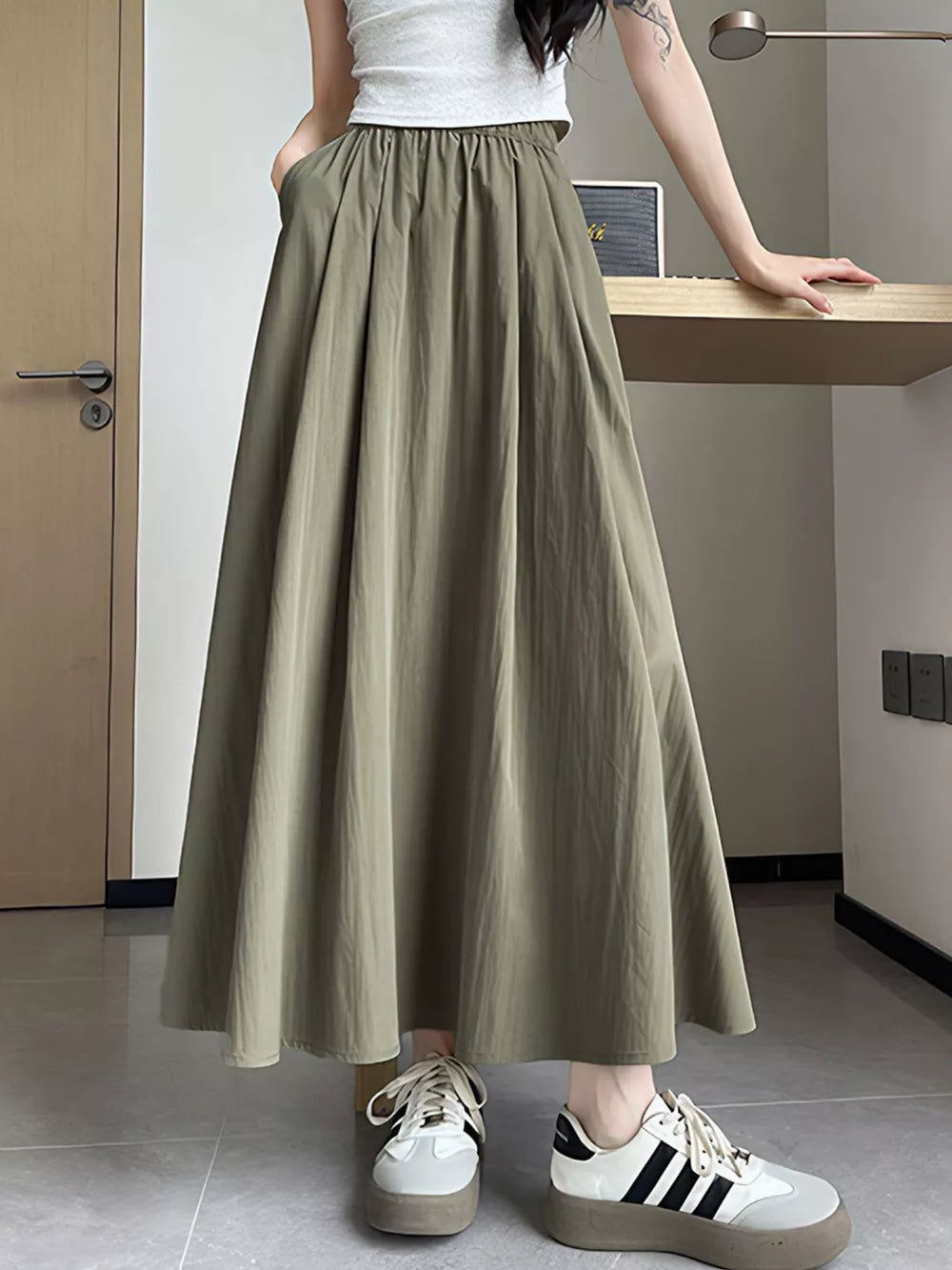 Olive green maxi skirt with pockets, flowing A-line cut, elastic waist, styled with sneakers.