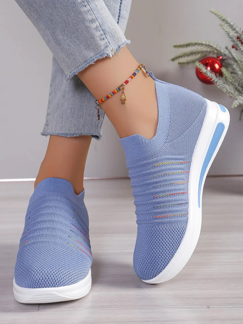 Light blue knit slip-on wedge sneakers with subtle rainbow stripes and white soles.