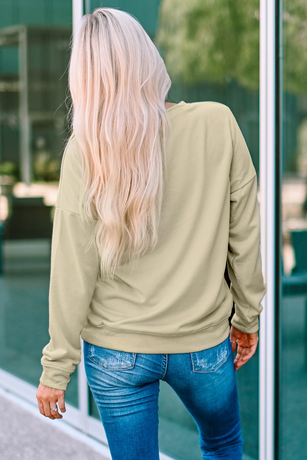 Khaki crewneck sweatshirt with long sleeves and ribbed cuffs, worn with blue jeans.