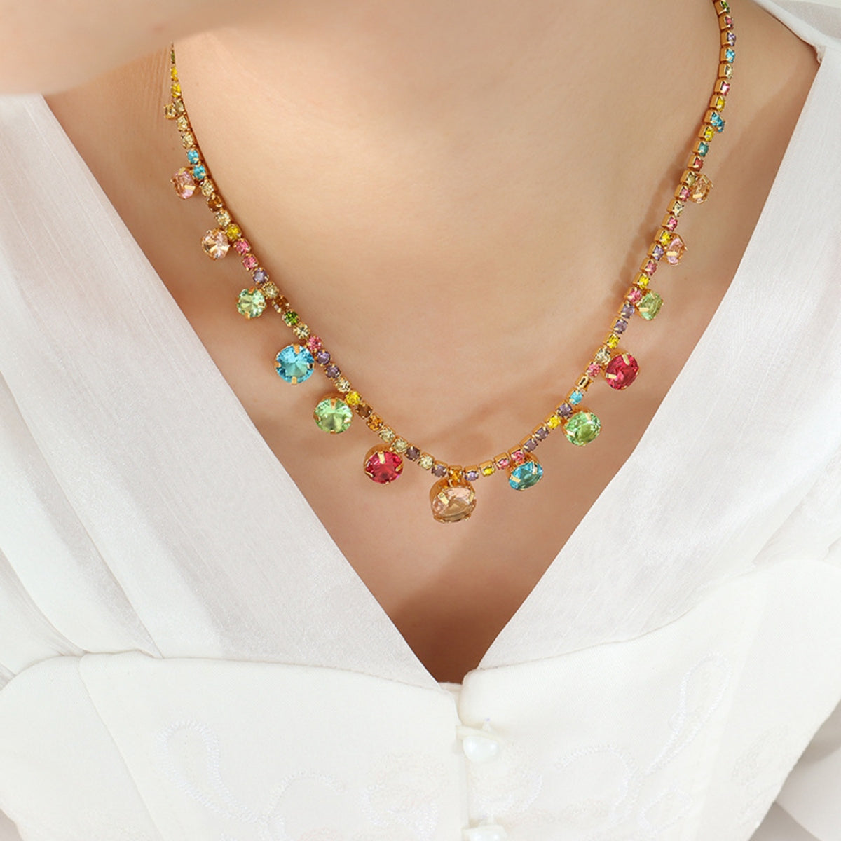 Gold chain necklace with colorful cascading gemstones and a v-neck white top.