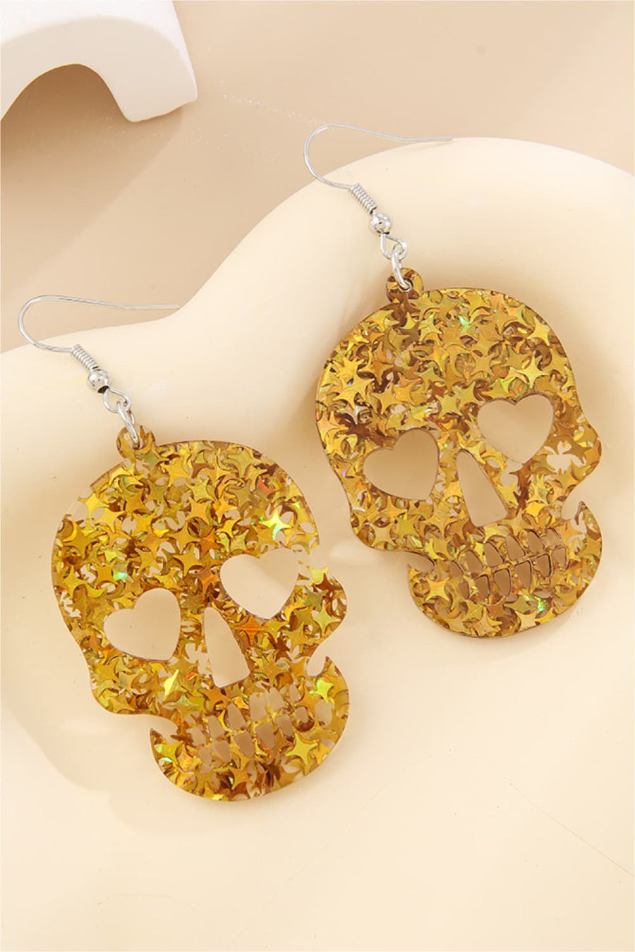 Gold glitter starburst skull dangle earrings with heart eye cutouts.