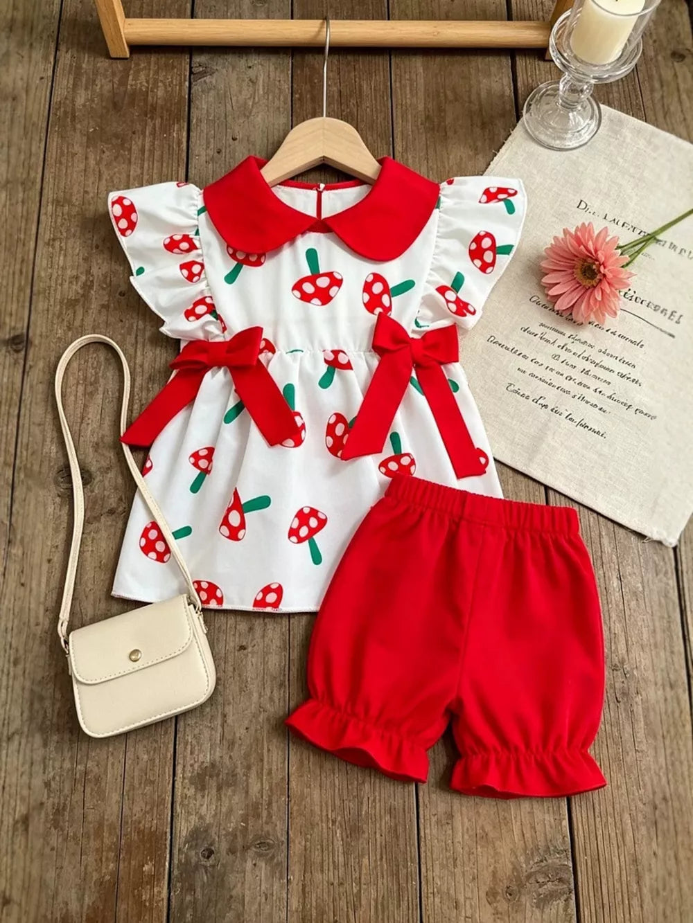 Baby set with white mushroom print dress and red bloomers, featuring red collar and bows.
