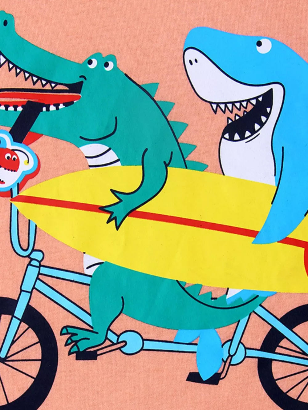 Kids graphic tee with a green alligator and blue shark riding a bike with a surfboard.