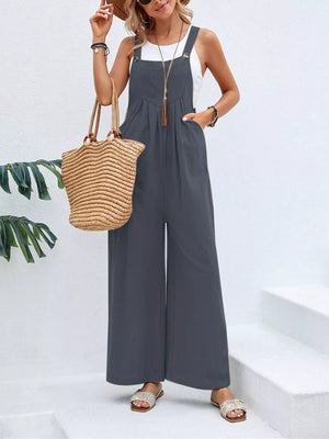 Dark gray wide-leg romper with adjustable straps and pockets, styled with a white tank and straw bag.