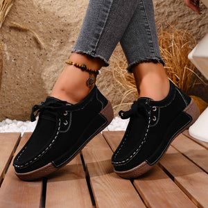 Black lace-up moccasin style sneakers with white stitching detail and brown sole.