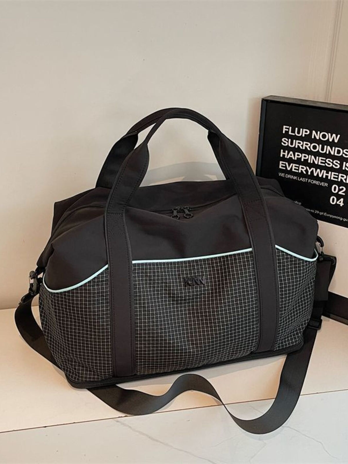 Black nylon duffel bag with grid pattern, light blue trim, and detachable strap.