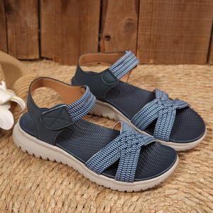 Blue woven strap open-toe flat sandals with adjustable ankle strap and knotted toe detail.