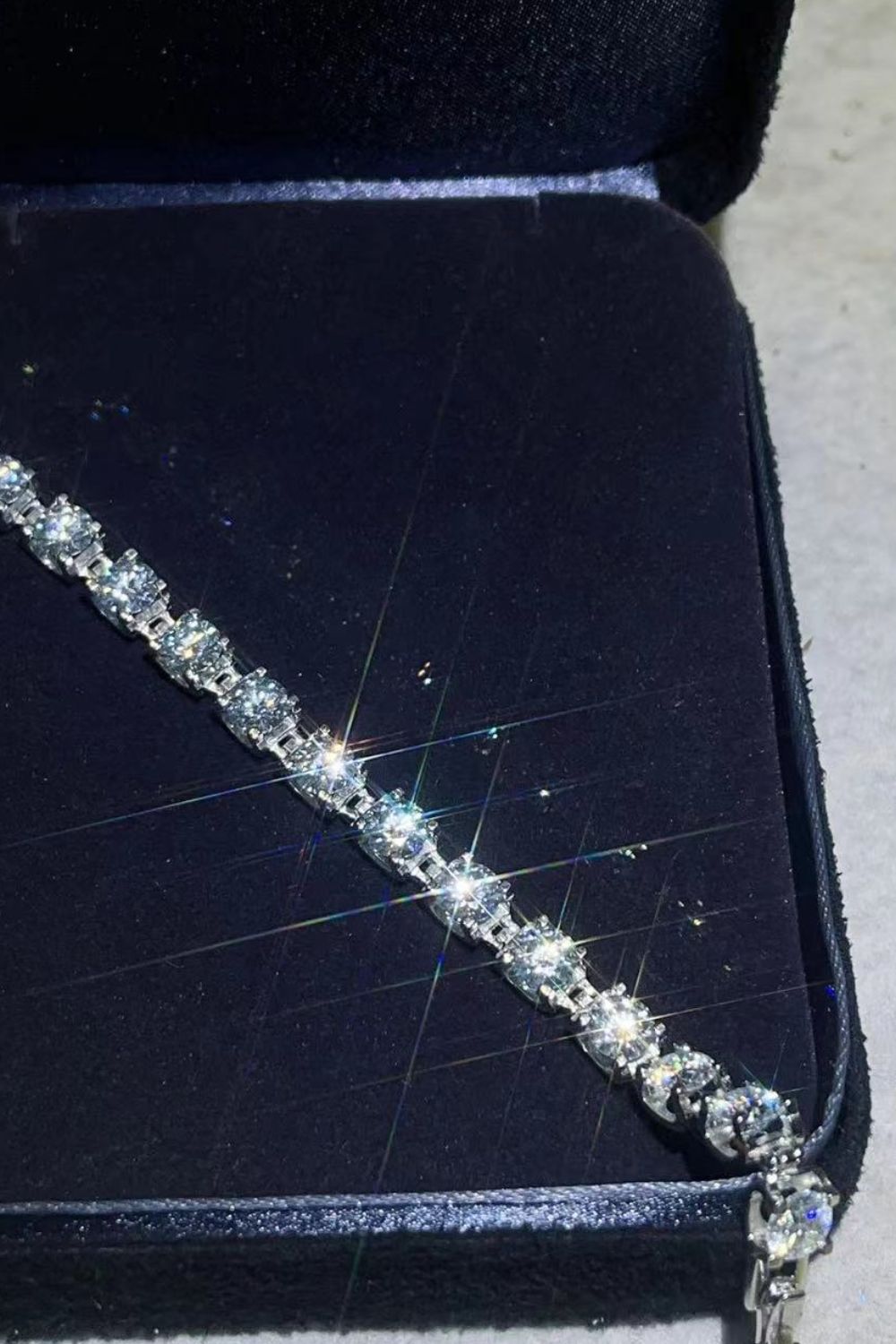 Diamond tennis bracelet in platinum with sparkling stones, presented in a dark jewelry box.