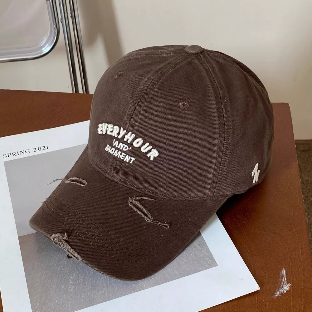Brown distressed baseball cap with white embroidered text and frayed details.