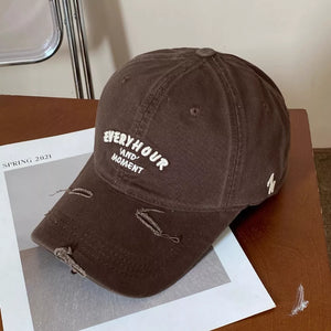 Brown distressed baseball cap with white embroidered text and frayed details.